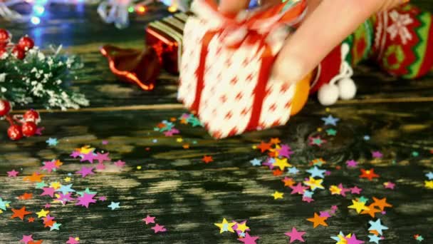 Mano pone caja de regalo de lazo rojo en la mesa, decorado con cosas de Navidad, en la guirnalda bokeh. — Vídeo de stock