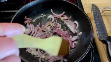 İnsan eli, mutfakta fırında yemek pişirmek için tavada kızarmış soğan karıştırıyor..