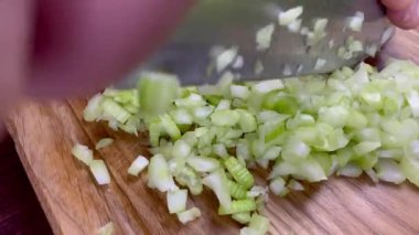 Chef hands chop finely raw celery stalk on wooden cutting board with kitchen knife. Slow motion.