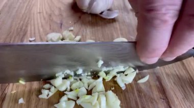 Aşçı elleri, ahşap kesme tahtasının üzerinde mutfak bıçağıyla çiğ sarımsak doğruyor. Yavaş çekim.