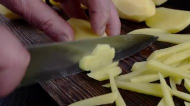 Chef hands cut raw potato into strip on wooden cutting board with kitchen knife.