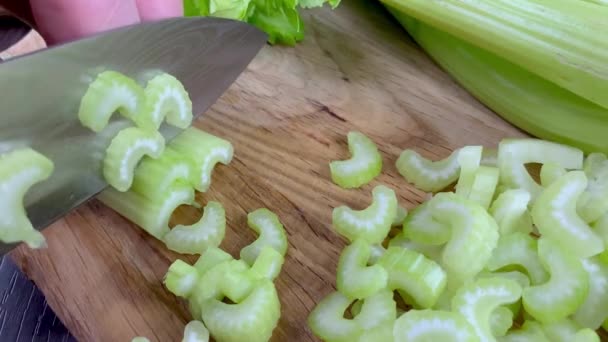Chef hands chop finely raw celery stalk on wooden cutting board with kitchen knife. Slow motion. — Stock video
