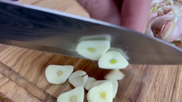 Chef-kok handen hakken fijn rauwe knoflook op houten snijplank met keukenmes. Langzame beweging. — Stockvideo