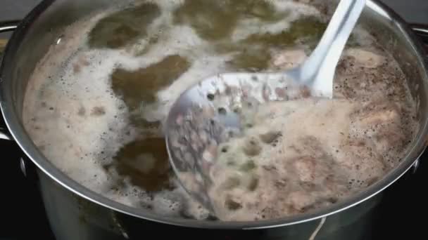 O caldo de carne com fervuras de espuma abundantes na panela, espuma retira-se com a colher de fenda metálica. — Vídeo de Stock