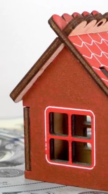 Dolar banknotlarının arka planında duran ve yavaşça dönen küçük aile evi modeli.