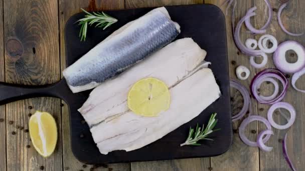 Filete de arenque salado con cebolla, limón y romero sobre tabla de cortar oscura giratoria. — Vídeos de Stock