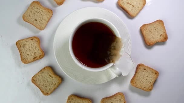 Kopje thee met theezakje en veel witte krokante crackers roteert langzaam op een lichte achtergrond. — Stockvideo