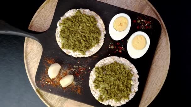 Tostadas de pastel de arroz con salsa de pesto verde y huevos cocidos rotan lentamente en la tabla de cortar. — Vídeo de stock