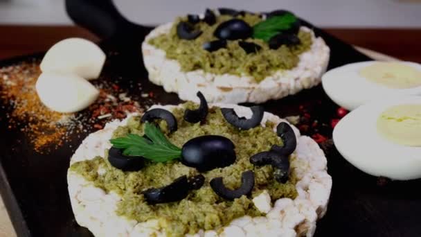 Rijstkoek toast met het verspreiden van groene pesto saus en gekookte eieren langzaam draaien op snijplank. — Stockvideo