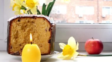 Evde yanan mum ve penceresinde taze nergis bulunan geleneksel Paskalya pastası dilimlenmiş. Geleneksel tatil yemekleri. Yakın plan..