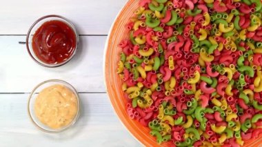 Multicolored uncooked raw italian pipe pasta rotating slowly on turntable in dish.