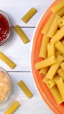 Pişmemiş çiğ italyan rigatoni makarnası. Tabakta yavaşça dönüyor. Beyaz ahşap arka planda. Dikey. Üst Manzara. Yakın plan..
