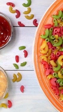 Çok renkli pişmemiş çiğ İtalyan pipo makarna döner döner döner döner döner tabakta. Beyaz ahşap arka planda. Dikey. Üst Manzara. Yakın plan..