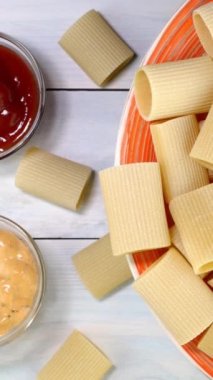 Pişmemiş çiğ İtalyan Paccheri makarnası. Tabakta yavaşça dönüyor. Beyaz ahşap arka planda. Dikey. Üst Manzara. Yakın plan..
