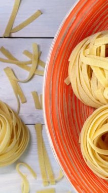 Pişmemiş çiğ İtalyan tagliatelle makarnası. Pikapta yavaşça dönüyor. Beyaz ahşap arka planda. Dikey. Üst Manzara. Yakın plan..