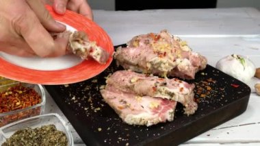 The cook puts fresh raw pork fillet with grated garlic and spices on plate for cooking chops.