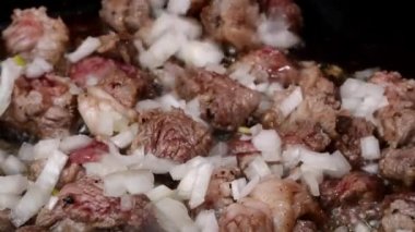Pieces chopped pork meat fried in hot frying pan with sliced onion, mixed with wooden spatula.