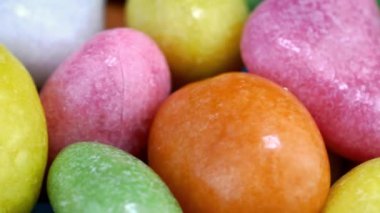 Pile of many round chewy candies dragee in multicolored glaze rotate slowly on turntable.