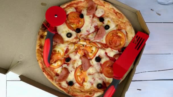 Свежая круглая пицца с помидорами, колбасой, моцареллой и оливками в картонной коробке медленно вращается. — стоковое видео