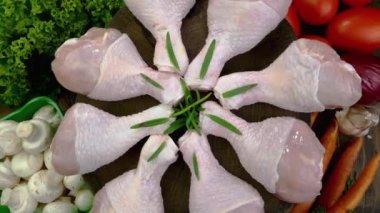 Fresh raw chicken drumsticks with rosemary twigs and vegetable rotating slowly on turntable. Food background on domestic kitchen. Close-up.