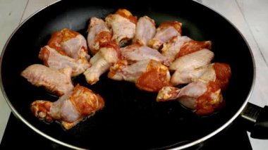 Chef places many sprinkled with spices sliced chicken wings in hot frying pan for preparation. Cooking tasty healthy dinner on domestic kitchen. Close up.