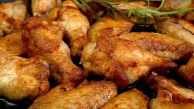 Many fried, sliced chicken wings with basil twig, with crispy crust rotate slowly. Cooking tasty healthy dinner on domestic kitchen. Close up.