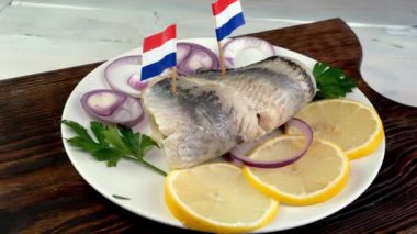Tasty salted herring fish fillet with onion rings, lemon, parsley and netherland flag rotate. Traditional healthy snack. Close up.