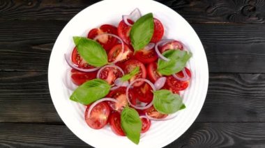 Tomato salad with basil and chopped onion in white ceramic dish rotate slowly. Tasty healthy vegetarian and vegan snack. Top view. Close up.