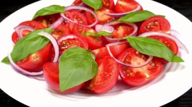 Tomato salad with basil and chopped onion in white ceramic dish rotate slowly. Tasty healthy vegetarian and vegan snack. Close up.