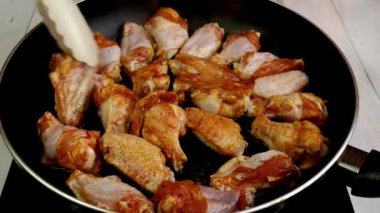 Many sprinkled with spices sliced chicken wings, preparation and turning in hot frying pan. Cooking tasty healthy dinner on domestic kitchen. Close up.