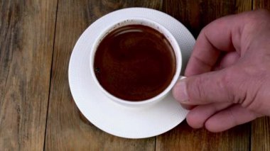 Koyu kahve espresso karıştıran çay kaşığı, ahşap masada beyaz bardakta kalın köpüklü. Kahve saatinde kahve yapmak. Kapat..