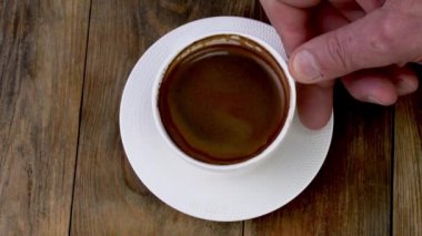 Koyu kahve espresso karıştıran çay kaşığı, ahşap masada beyaz bardakta kalın köpüklü. Kahve saatinde kahve yapmak. Kapat..