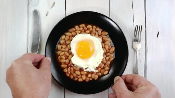 黄身と焼き豆と揚げ卵を木製のキッチンテーブルの上に黒いプレートに回します おいしい健康的な自家製ベジタリアン料理 閉じろ — ストック動画