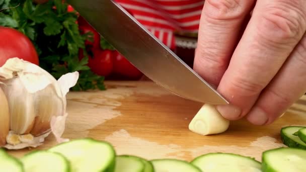 国産キッチンの木製まな板に鋭利なナイフでニンニクをスライス おいしいベジタリアンやビーガン健康野菜サラダを準備します スローモーション 閉じろ — ストック動画