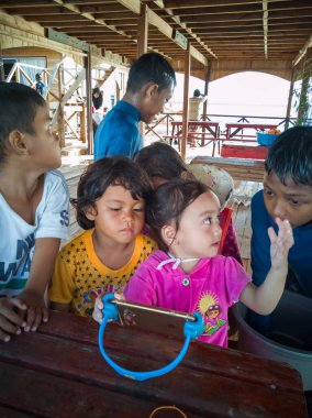 Semporna, Malezya - 26 Kasım 2019: Çocuklar cep telefonunda video izliyorlar. Teknoloji kullanan çocuklar.