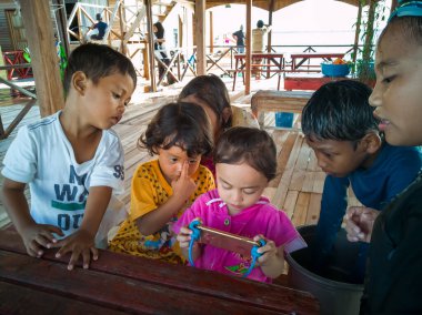 Semporna, Malezya - 26 Kasım 2019: Çocuklar cep telefonunda video izliyorlar. Teknoloji kullanan çocuklar.