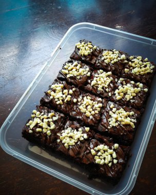 Tahta arka planda, üzerinde badem uçları, ev yapımı fırın ve tatlı olan plastik bir kapta çikolatalı brownie.