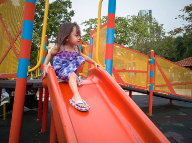 Küçük kız oyun parkında kaydırağın üstünde oynuyor.