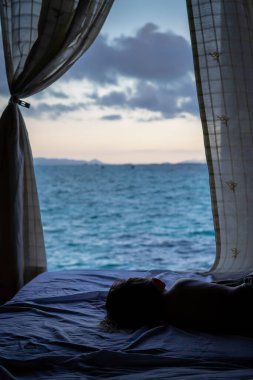 Deniz manzaralı arka plan, çocuklar yatağın üzerinde uyur ve suya bakar..