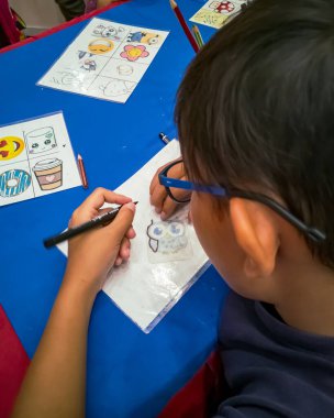 Kuala Lumpur, Malezya - Kasım 2019: Geri dönüşümlü plastik bir konteynır örtüsüne çizim yapan genç bir çocuğun yüksek açılı yakın çekimi. Anahtarlık yapıyorum..