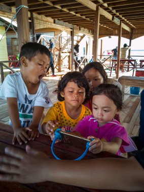 Semporna, Malezya - 26 Kasım 2019: Çocuklar cep telefonunda video izliyorlar. Teknoloji kullanan çocuklar.