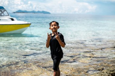 Genç çocuk mutlu ve kumsalda barış işareti gösteriyor..
