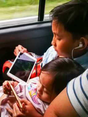 Kuala Lumpur, Malezya - 24 Kasım 2019: Arabada dijital cihazlarla oynayan kız ve erkek kardeş.
