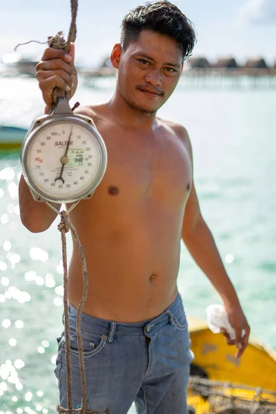 Semporna, Malezya - 26 Kasım 2019: Yerel adam Bum Bum Adası 'ndaki balıkçıdan satın alırken balık ağırlığı tartısını tutuyor.