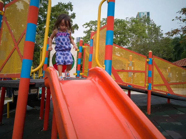 Küçük kız oyun parkında kaydırağın üstünde oynuyor.