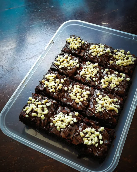 Tahta arka planda, üzerinde badem uçları, ev yapımı fırın ve tatlı olan plastik bir kapta çikolatalı brownie.