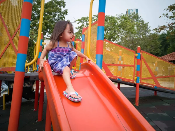 Küçük kız oyun parkında kaydırağın üstünde oynuyor.
