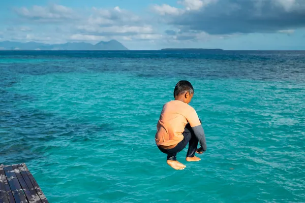 Çocuklar tahta bir iskeleden suya atlıyorlar..