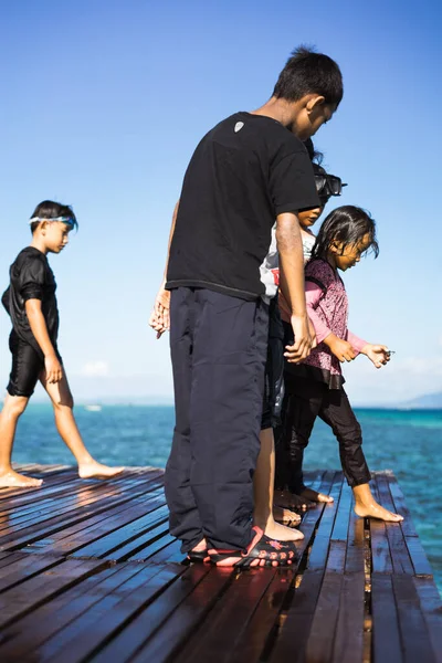 Semporna, Malezya - 26 Kasım 2019: Çocuklar suya atlamadan önce ahşap iskelede duruyorlar.