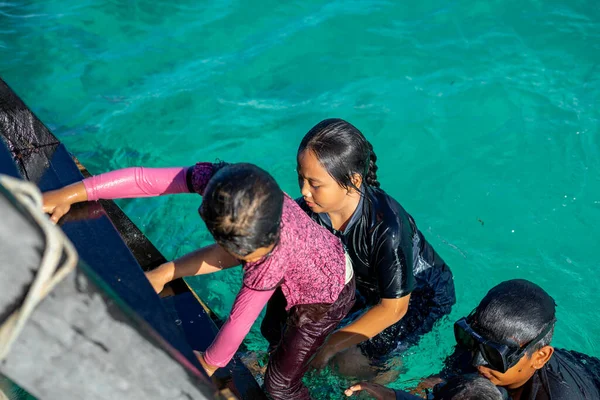 Semporna, Malezya - 26 Kasım 2019: Çocuklar eğlence için kristal berrak mavi okyanusa atladıktan sonra bir iskelede merdivene tırmandılar.